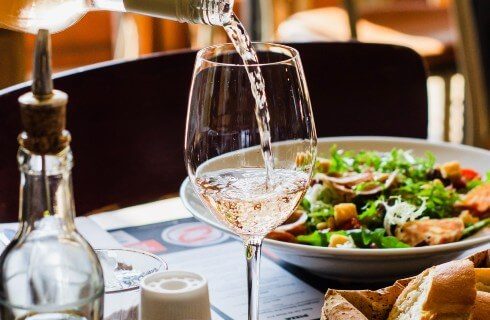 Restaurant table with bowl of salad and wine being poured into a wine glass