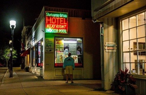 A main street at night with a large square green and red neon sign