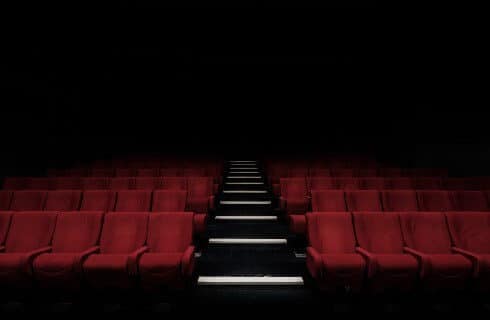 Dark empty theater with one aisle of stairs between dark red seats