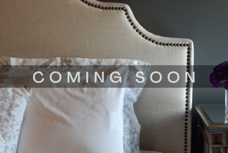 Bed with table holding vase of flowers with coming soon label across image