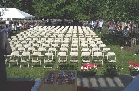 Outdoor lawn area with rows of white chairs set up by a white tent for an event