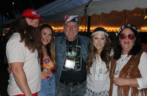 A group of five people gathered together wearing 70's hippy clothing