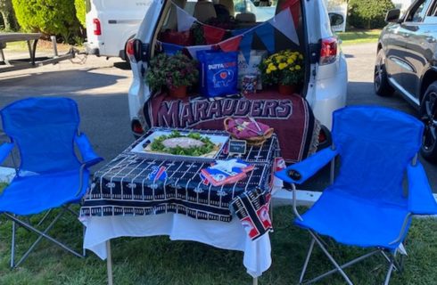 Tailgate party with back of an open van decorated and table with two lawn chairs