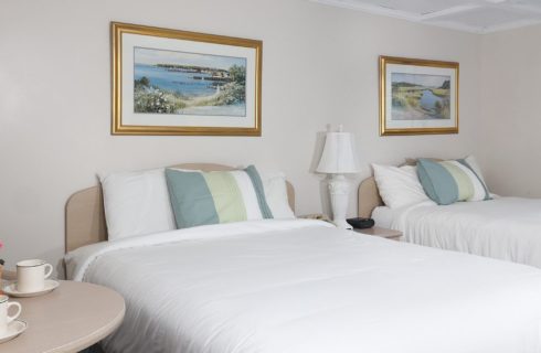 Bedroom with two queen beds, artwork with gold frames and table with flowers and two coffee cups with saucers