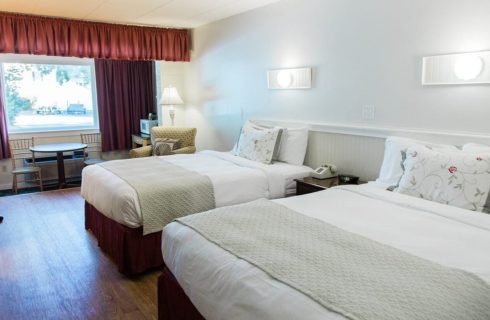 Bedroom with two queen beds, round table with two chairs in front of large window with red curtains