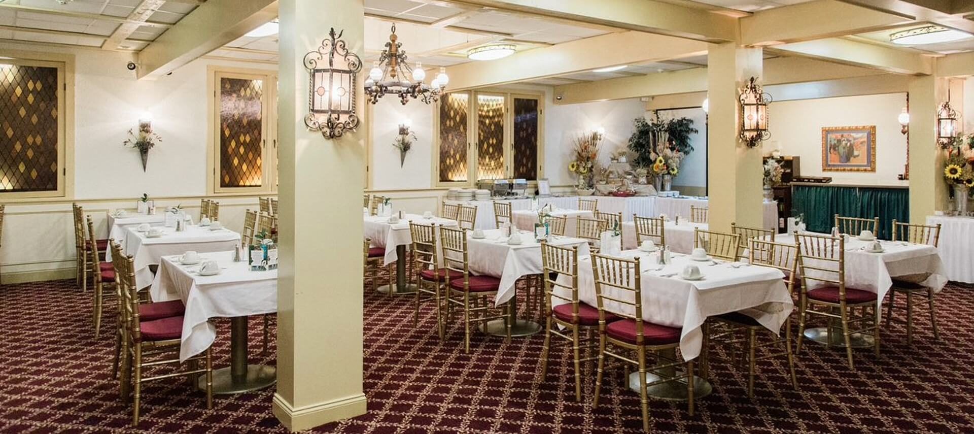 Large dining room with columns, patterned carpet and white tables with red and gold chairs