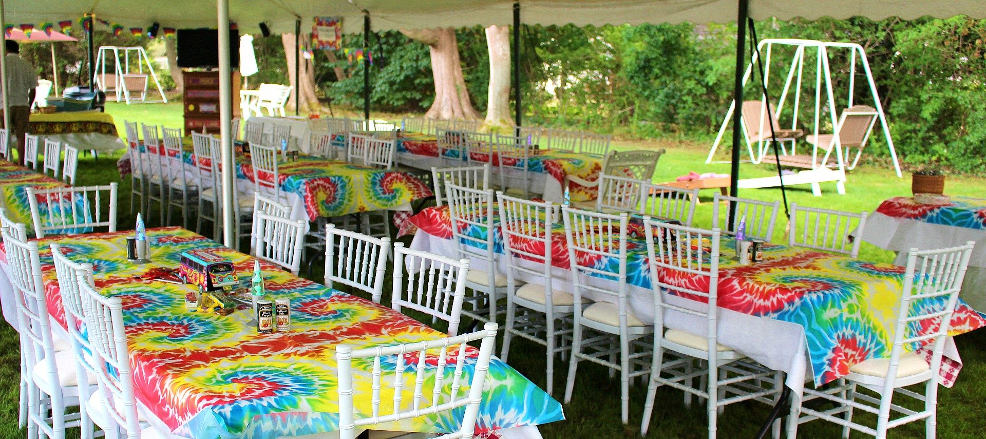 outdoor tented event with several tables set up in tie-dyed table cloths