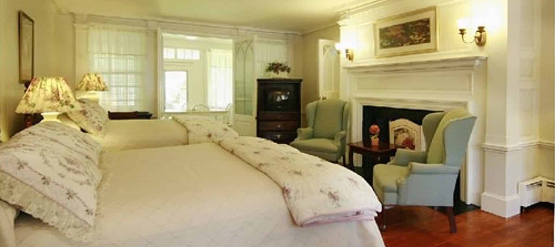 Bedroom with two queen beds, large fireplace, wingback sitting chairs and antique hutch
