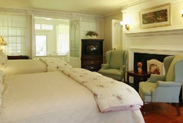 Bedroom with two queen beds, large fireplace, wingback sitting chairs and antique hutch