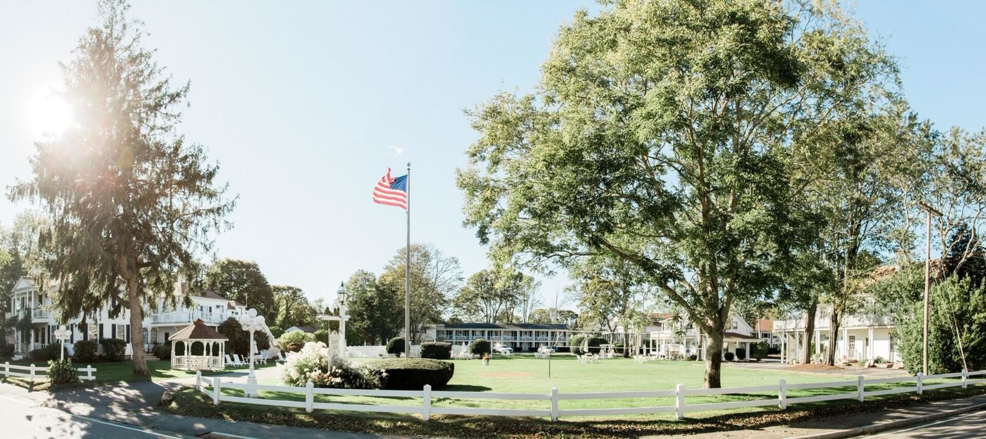 Panoramic view of hotel grounds with several buildings, large grassy area, trees and center flag pole with American flag