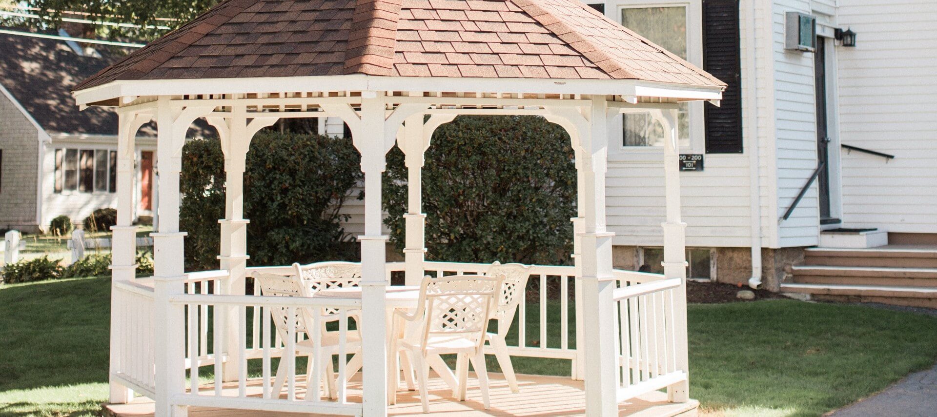 A white gazebo with brown roof with a table and chairs inside