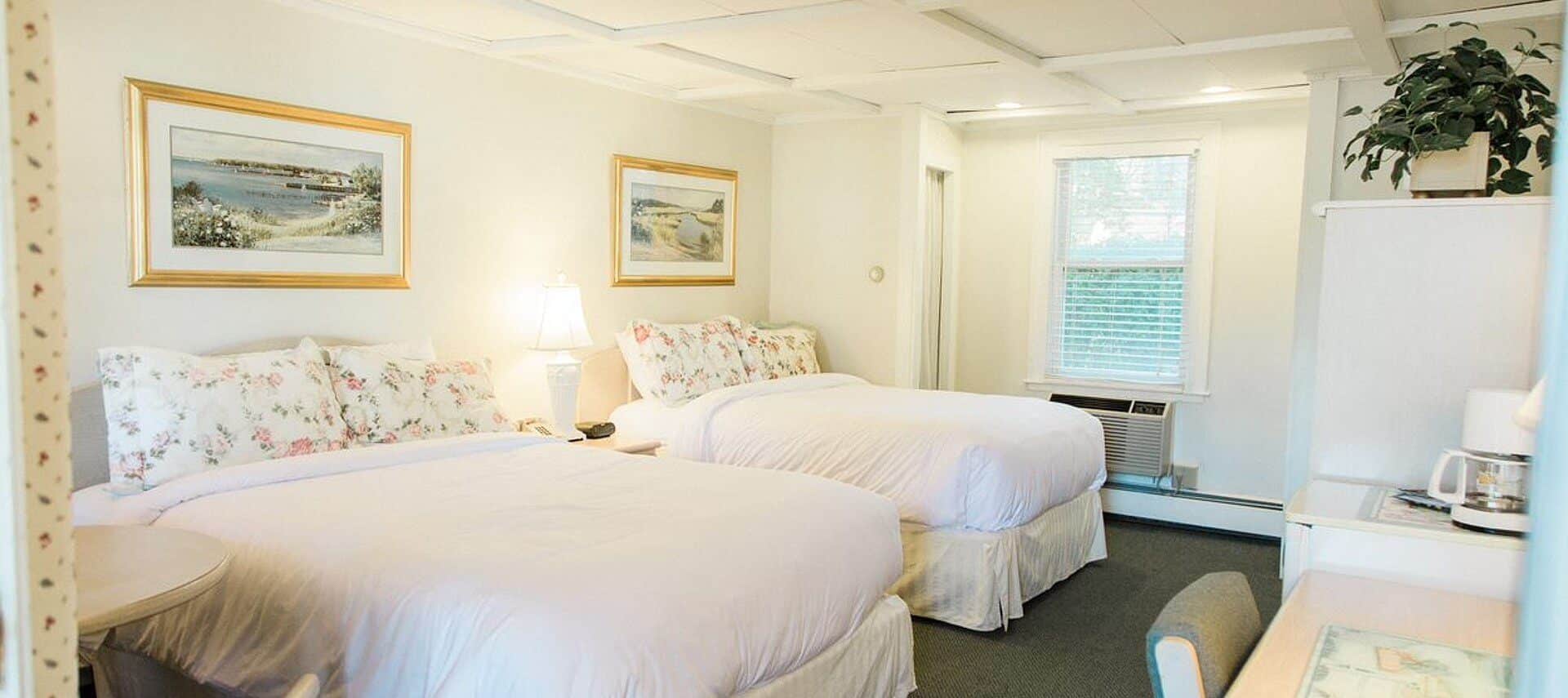 Bedroom in white and florals with two queen beds, desk with chair and artwork with gold frames