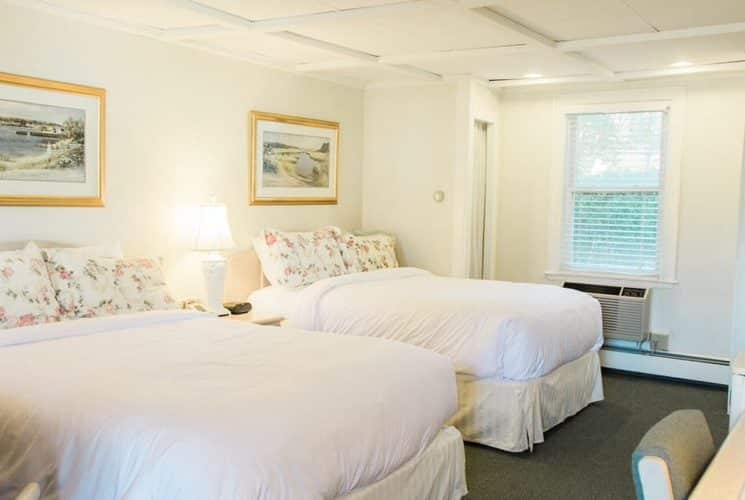 Bedroom in white and florals with two queen beds, desk with chair and artwork with gold frames