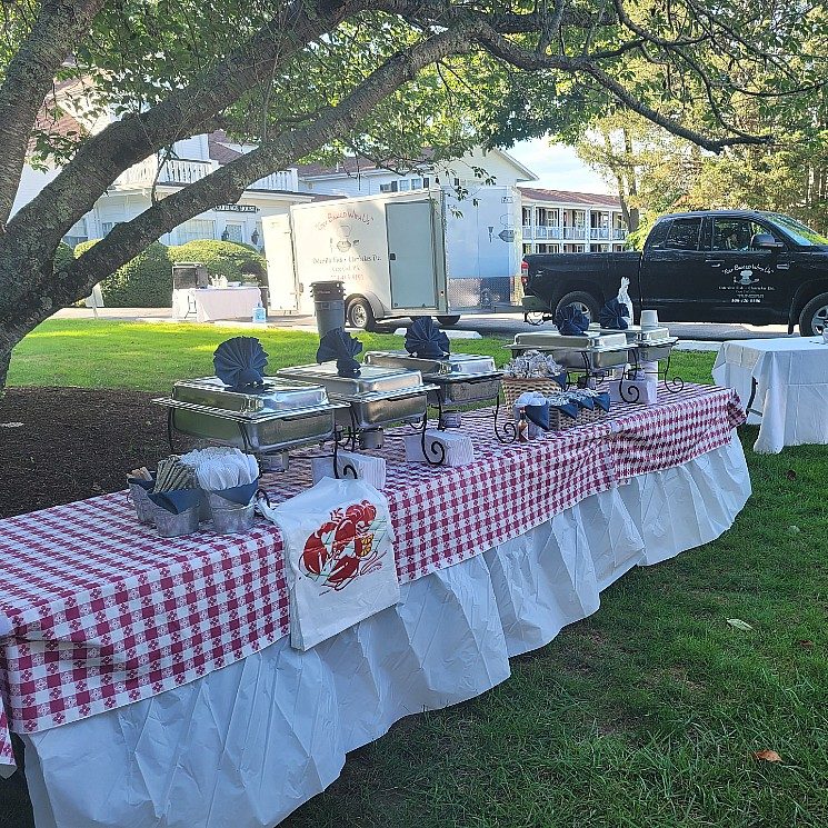 Outdoor table set up with red and white checkered cloth and several silver warming dishes
