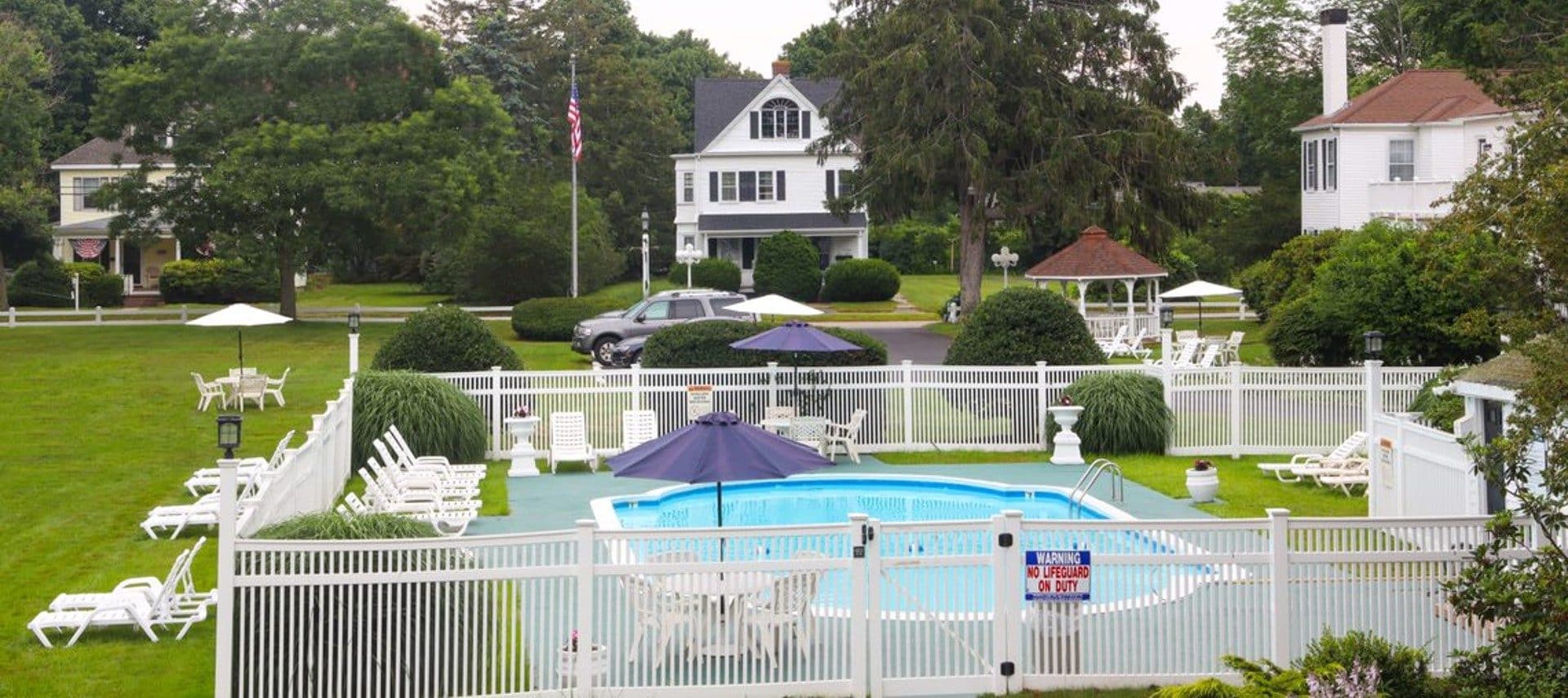Outdoor pool with white fence and lounging chairs surrounded by several homes