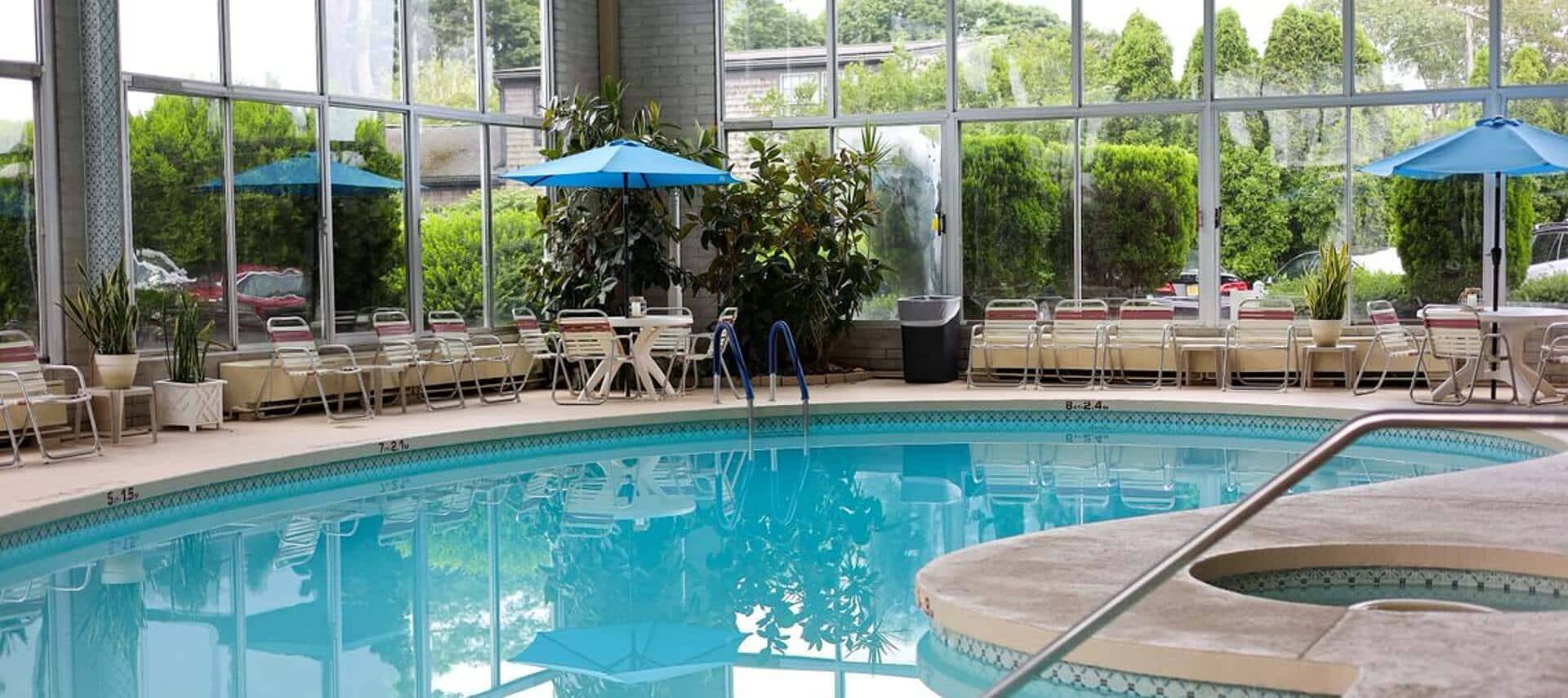 Large indoor pool with windows all around and chairs with blue patio umbrellas