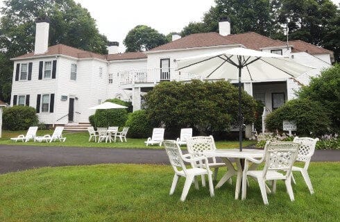 Outdoor lawn area in front of a large white building with patio tables and lounging chairs