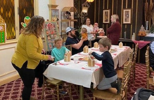 Group of adults and kids in a dining room making gingerbread houses
